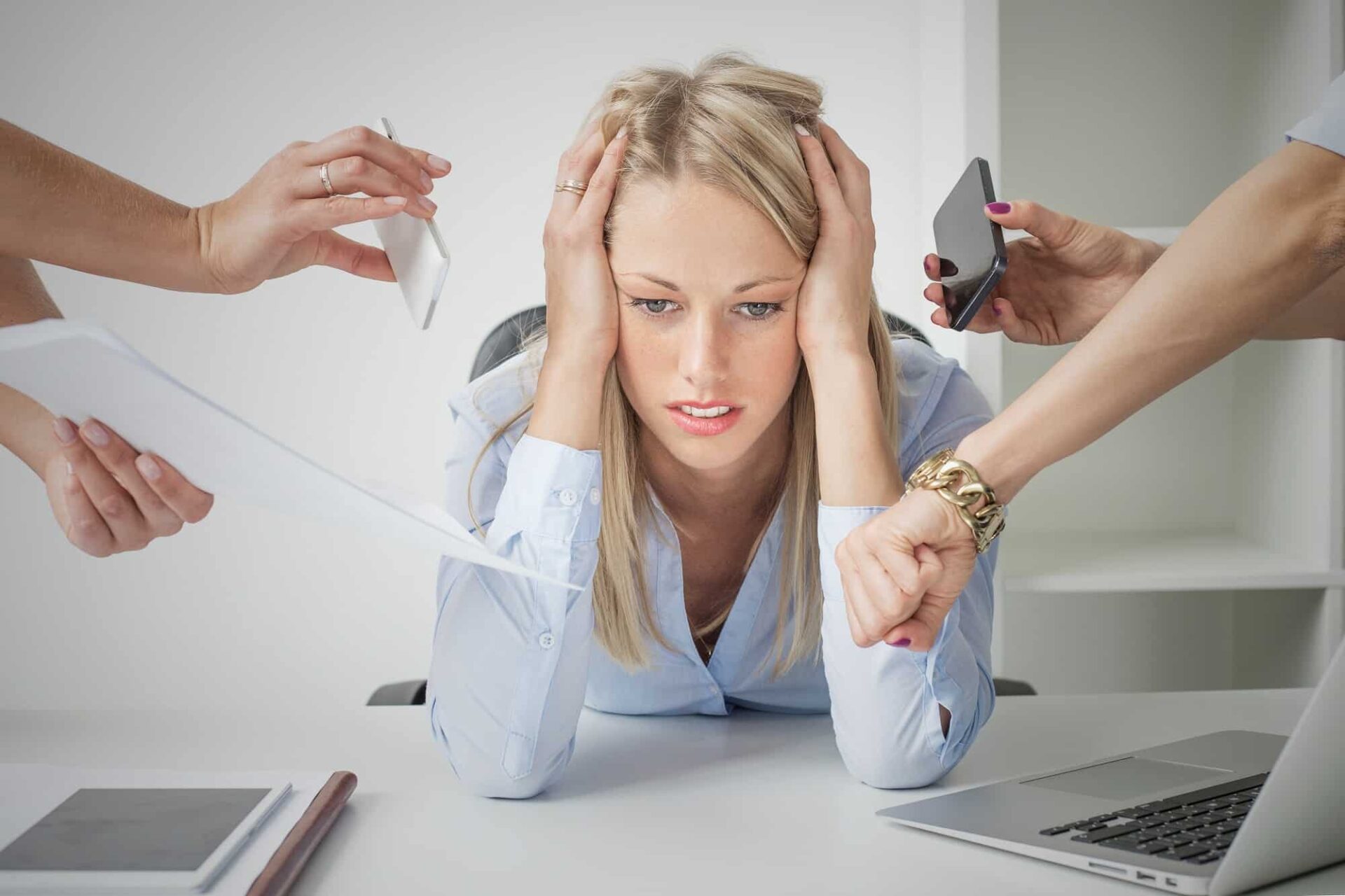 A stressed CEO overwhelmed by tasks, surrounded by hands holding phones and papers, illustrating the need for a fractional COO to bring clarity and efficiency.